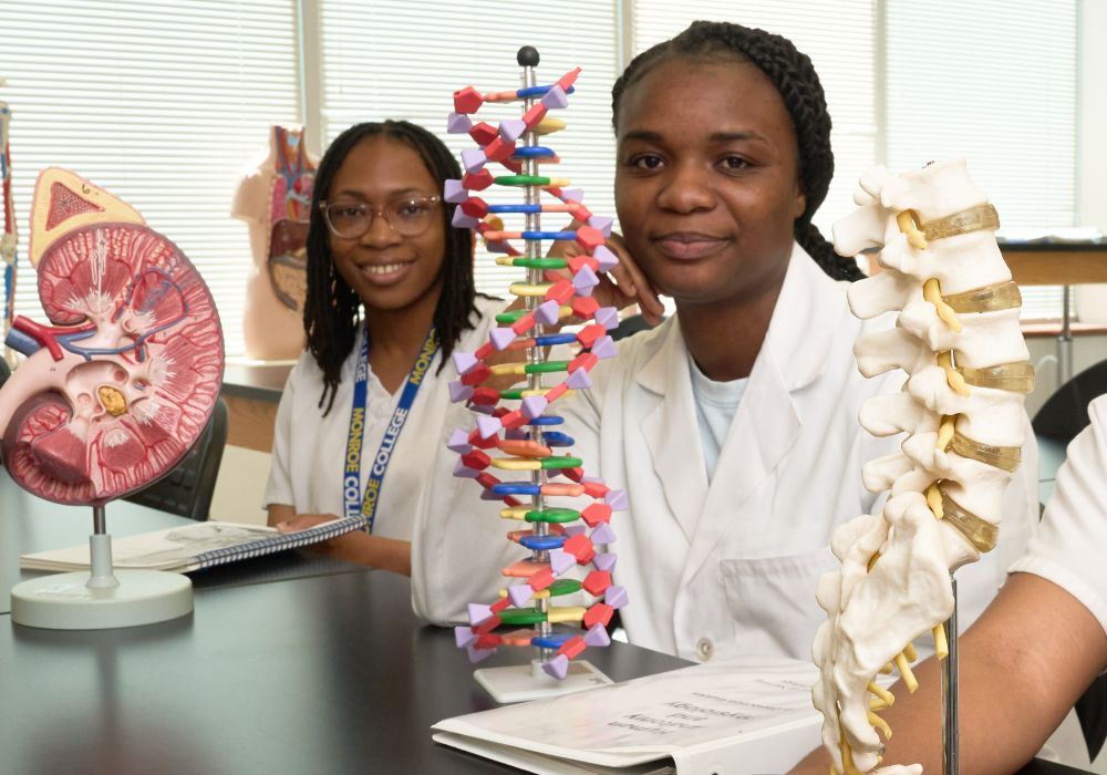 Three women in lab coats while displaying a model of human DNA.